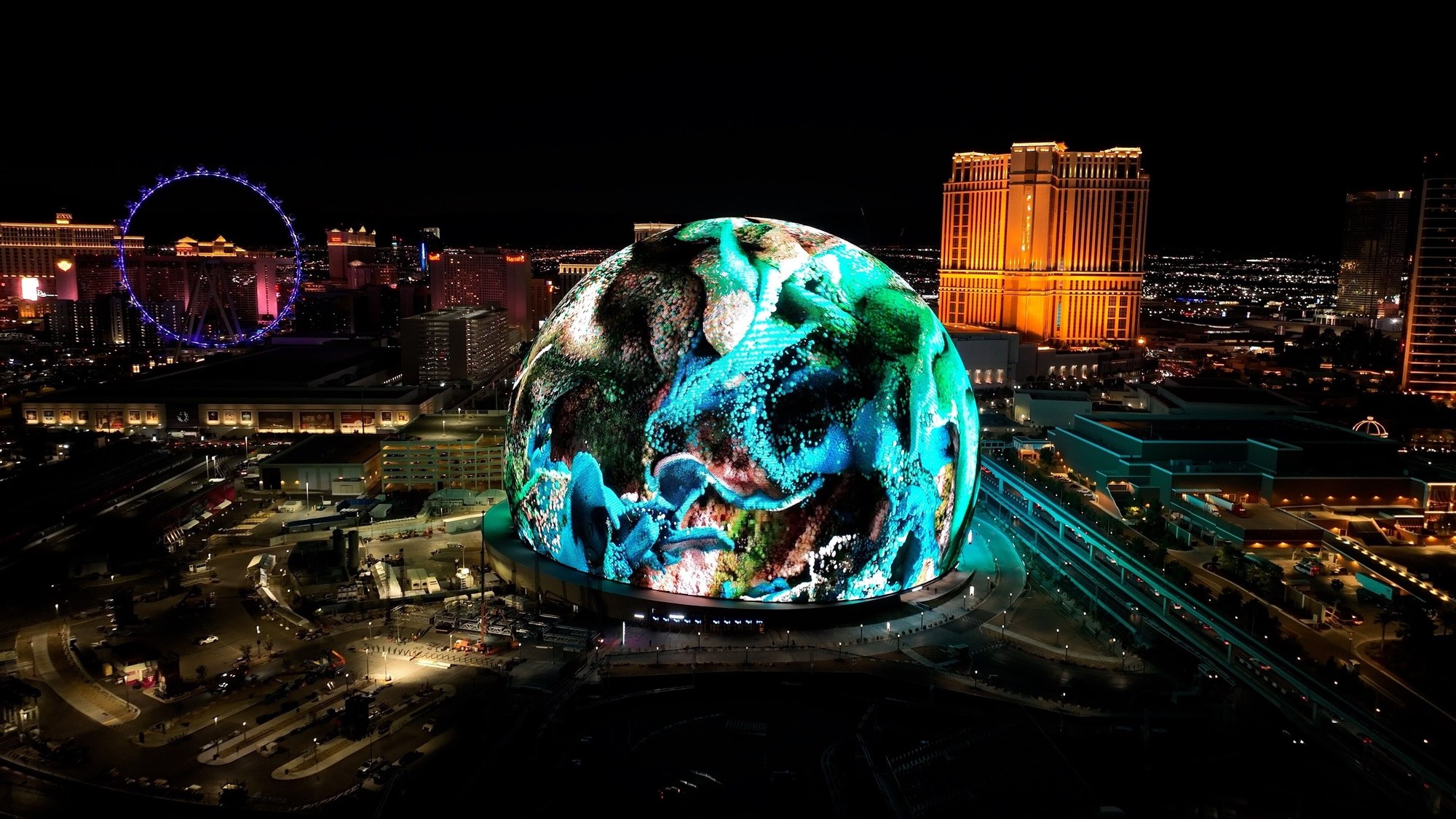Sphere lit up at night between the High Roller and the Venetian